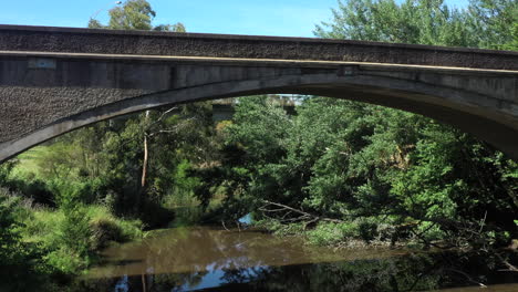 AERIAL-Under-Historic-Arch-Cement-Bridge-Over-A-River