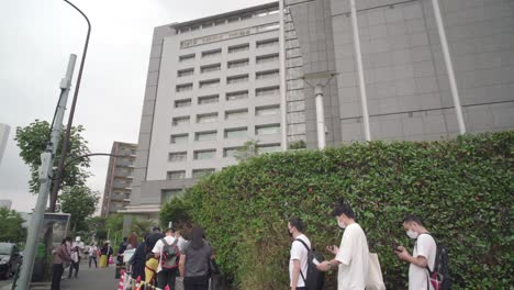Personas-Con-Mascarillas-Haciendo-Cola-Y-Manteniendo-El-Distanciamiento-Social-Fuera-Del-Edificio-De-La-Oficina-Regional-De-Inmigración-Durante-El-Brote-Pandémico-De-Covid-19-En-Tokio,-Japón