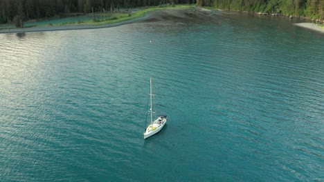 Weißes-Segelboot,-Das-Auf-Einem-Ruhigen-See-Mit-Wald-Auf-Einem-Berg-In-Alaska-Schwimmt