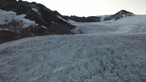 Interesting-and-beautiful-patterns,-lines-and-cracks-in-the-ice-of-the-glacier-on-top-of-the-swiss-alps-mountain-during-a-sunrise-or-sunset-in-the-background