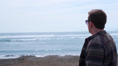 young-man-looking-at-the-sea-on-a-sunny-day-with-beautiful-waves-in-camaralenta,-pichilemu,-punta-de-lobos,-Chile