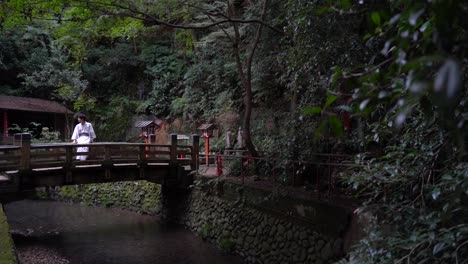 Slow-reveal-of-man-in-typical-Japanese-Kimono-clothing-standing-on-bridge-of-small-shrine-in-forest