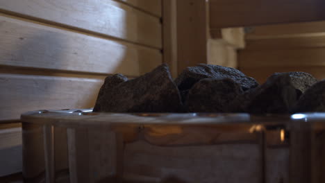 Water-pouring-over-steamy-rocks-of-wood-stove-in-Finnish-sauna,-close-up-shot