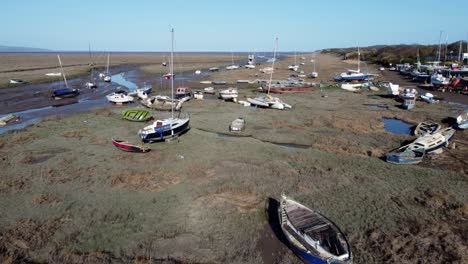 Various-stranded-anchored-fishing-boats-shipyard-in-marsh-mud-low-tide-coastline-aerial-flyover-view