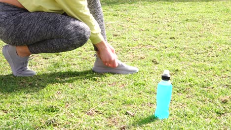 athlete-tying-sneakers-on-grass-with-isotonic-drink-next-to