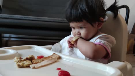 Linda-Niña-Asiática-Comiendo-Su-Comida-Casera-En-Una-Silla-De-Alimentación-Para-Bebés