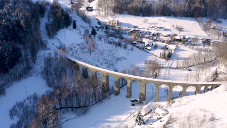 Stone-train-viaduct-railroad-around-a-small-village-in-winter-snow