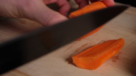 Chef-hands-cuts-carrots-pieces-in-half-on-wood-chopping-board