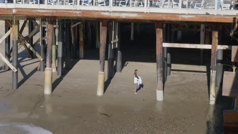 Panning-shot-of-a-girl-under-a-pier-up-to-the-restaurant-patio-above