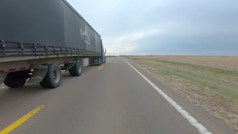 Point-of-view-driving-on-a-straight-stretch-of-country-highway,vehicle-is-passed-by-a-large-blue-semi-truck