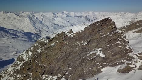 Majestic-exposed-Mountains-rising-through-the-snow-surrounding-in-Val-Thorens,-French-Alps---Aerial-ascending-parallax-revealing-shot