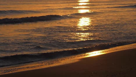 Golden-waves-reflecting-sunrise-gentle-lapping-onto-sandy-beach,-tropical-beach-paradise,-early-morning-shoreline