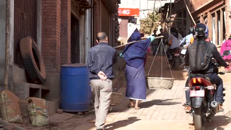 Newari-Old-woman-carries-baskets-in-crowded-Bhaktapur-street,-Nepal