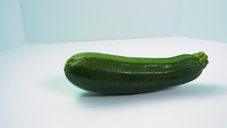 Green-fresh-zucchini-squash-rotates-on-a-light-blue-background,-healthy-food,-concept,-medium-close-up-shot-camera-rotate-left