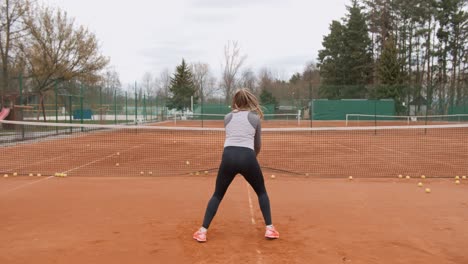 Rear-view-showing-female-tennis-player-defending-several-balls-near-net-during-training
