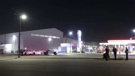 Wide-shot-of-the-crime-scene-with-tape-and-police-cars-parked-at-a-gas-station-at-night