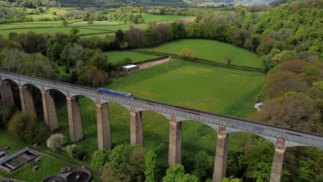 Aerial-view-following-narrow-boat-on-Trevor-basin-Pontcysyllte-aqueduct-crossing-in-Welsh-valley-countryside-rising-upwards-tilt-down