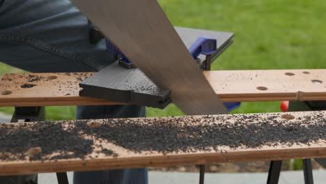 Cutting-composite-wood-with-a-hand-saw-on-a-workbench-at-home-outside