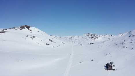 Ski-trails-with-unrecognisable-persons-in-Krossdalen-snowy-wilderness---Hardangervidda-Norway-reverse-aerial