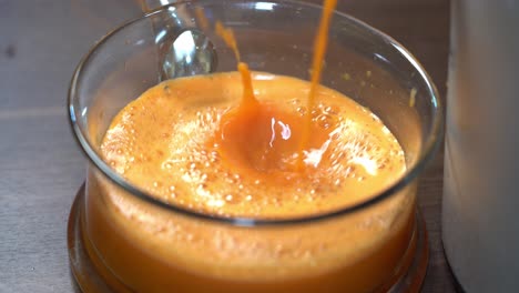 Fresh-orange-and-carrot-juice-pouring-from-juicer-into-glass-bowl---splashing-and-natural-foamy-fresh