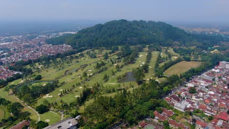 Aerial-view-of-green-field-of-golf-course-and-Tidar-Hill-in-Magelang,-Indonesia