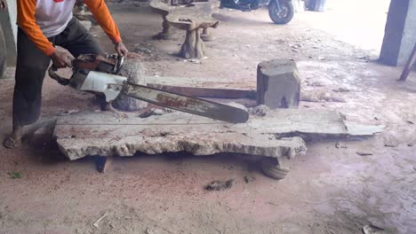 Worker-of-carpentry-workshop-in-dust-is-sawing-wooden-board-with-chainsaw
