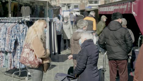 Old-woman-with-medical-mask-talks-with-young-masked-girl-at-the-market-as-they-wait-in-line-for-the-butcher---static-shot
