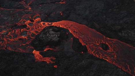 Red-lava-river-flowing-slowly-through-black-solidified-rocks