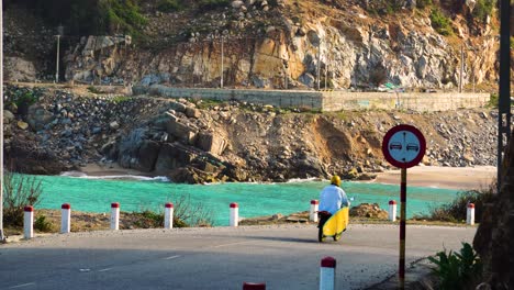 Surfer-driving-on-coastal-road-in-Vietnam-in-motorbike-with-yellow-board-on-rack