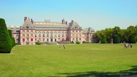 People-Walking-On-Green-Lawn-Of-International-University-City-Park-Of-Paris-With-Maison-Internationale-Student-Housing-In-France