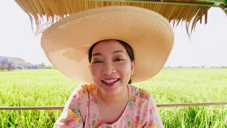 Schöne-Junge-Asiatische-Frau-Mit-Hut-Im-Reisfeld,-Die-Einen-Videoanruf-Tätigt