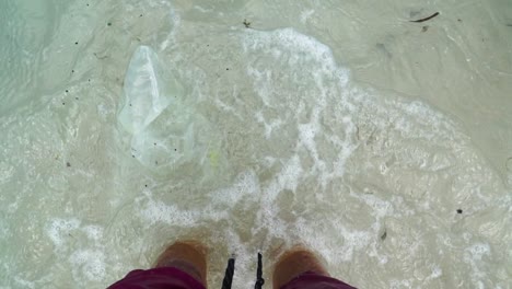 First-person-top-down-view-of-legs-and-polluted-sea-waves-washing-over-bare-feet