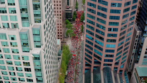 People-in-Orange-Shirts-fill-the-Street-to-Protest,-High-Drone-Shot-Moving-Forward