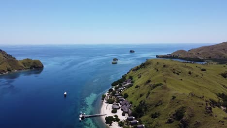 Pulau-Sebayur-island-Komodo-resort-in-Indonesia-with-boats-and-huts-near-the-main-pier,-Aerial-dolly-out-reveal-shot
