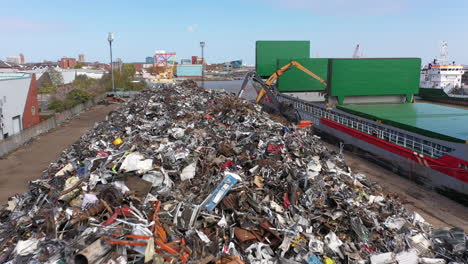 Footage-flies-over-a-large-mound-of-scrap-metal-while-two-grab-machines-grab-metal-and-load-it-onto-the-ship