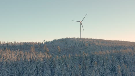 AERIAL---Wind-turbine-at-sunrise-in-a-snowy-forest-in-Sweden,-wide-shot-forward