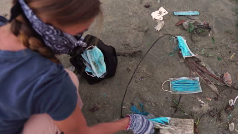 A-Woman-Picking-Up-Environmental-Waste-From-a-Beach-with-Used-and-Discarded-Covid-19-Facemasks