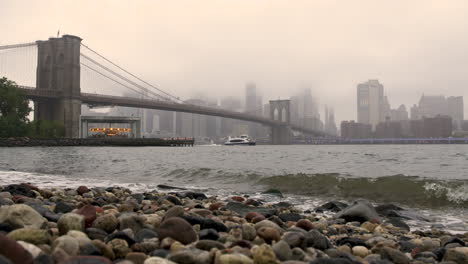 Waves-On-The-Shore-Of-The-East-River-With-Brooklyn-Bridge-And-Downtown-Manhattan-In-The-Distance,-NYC,-U