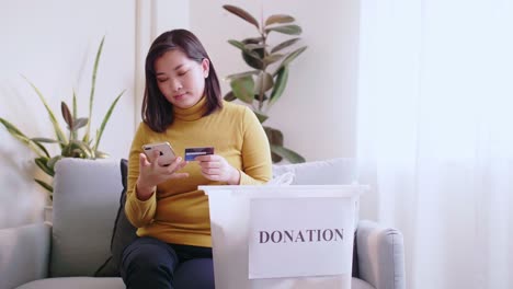 Frau-Drückt-Mit-Kreditkarte-Aufs-Telefon,-Um-Online-Zu-Bezahlen-Und-Die-Lieferung-Einer-Spendenbox-Zu-Reservieren