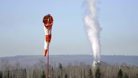 Windsock-At-Quesnel-Airport-With-Billowing-Steam-From-Industrial-Chimney-In-British-Columbia,-Canada