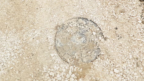 Round-Cast-Iron-Manhole-Lid-Covered-With-Stones-At-Road-Under-Construction-In-Leiria,-Portugal