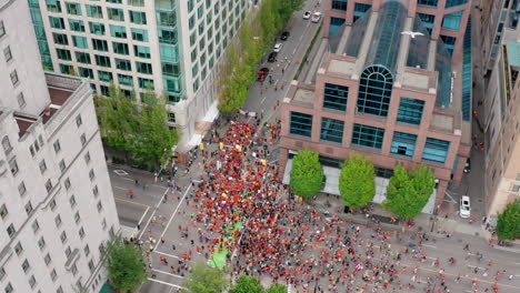 Huge-crowd-of-protesters-march-below,-rising-tilt-down-aerial-reveal-in-UHD