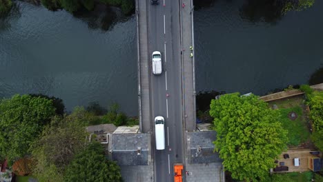 Top-down-aerial-of-signal-led-traffic-moving-in-single-file-across-an-old-victorian-road-bridgte-under-repair,-tolhouses-on-the-bridge