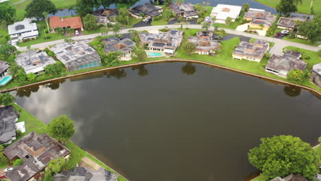 An-aerial-view-of-a-reflective-pond,-surrounded-by-nice-houses-and-green-grass-on-a-sunny-day