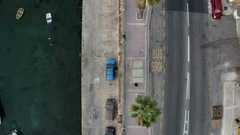 Overhead-shot-of-a-seaside-city-harbor-street-with-cars-and-bus-stop