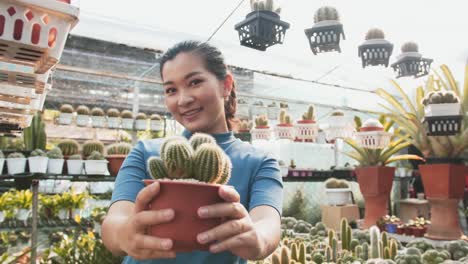 Portrait-of-beautiful-young-Asian-girl-showing-indoor-cactus-plant-in-flowerpot