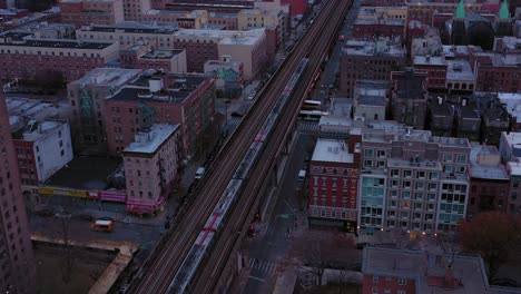 Aerial-trucking-shot-toward-a-commuter-train-moving-through-the-buildings-of-Harlem-New-York-City-just-after-daybreak