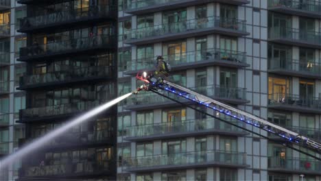 Solo-firefighter-in-action,-fighting-the-fire-on-top-of-the-aerial-hydraulic-ladder-apparatus-in-an-urban-skyscraper-environment
