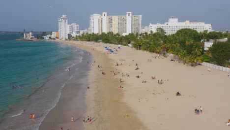 Una-Vista-Aérea-De-Una-Sección-Costera-De-San-Juan,-Puerto-Rico,-Con-Turistas-Descansando-En-La-Playa-Y-Complejos-Turísticos-Al-Fondo.