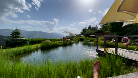 Pov-pan-shot-showing-resting-people-at-beautiful-natural-lake-during-blue-sky-and-sunlight-in-the-mountains